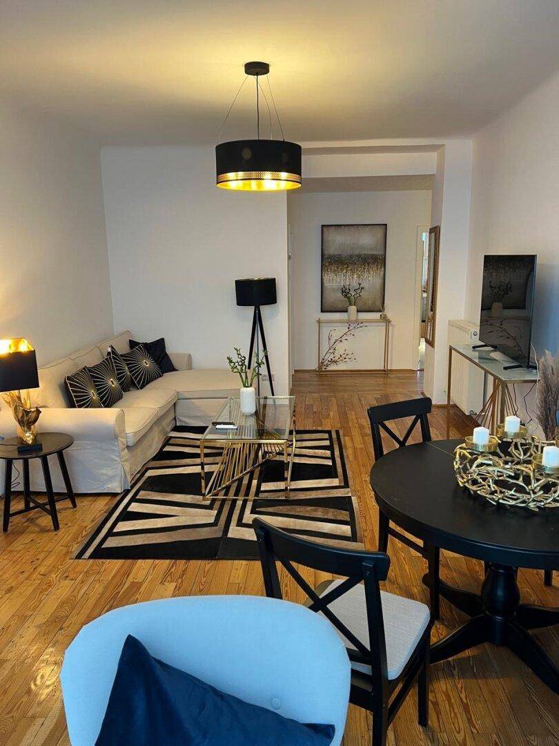 Offener Wohn- und Essbereich mit Holzboden, modernem Sofa und schwarzem Esstisch.