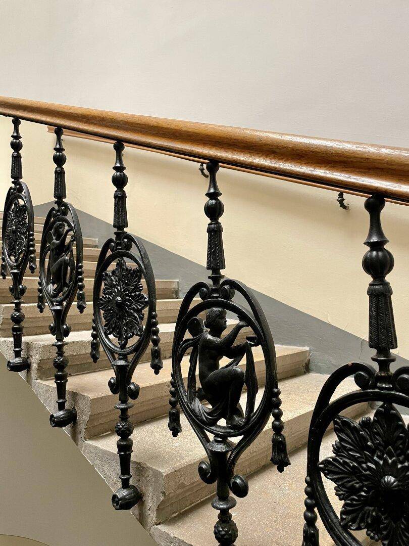 Elegantes Treppenhaus mit kunstvollem schmiedeeisernem Geländer und Holzhandlauf in einem Altbau.
