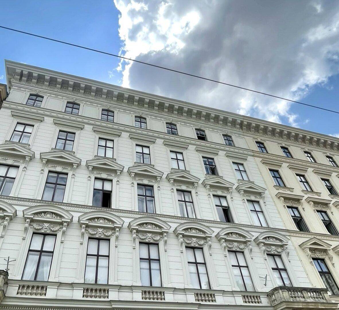 Historische Fassade eines eleganten Gebäudes mit zahlreichen Fenstern und dekorativen Stuckelementen unter blauem Himmel.