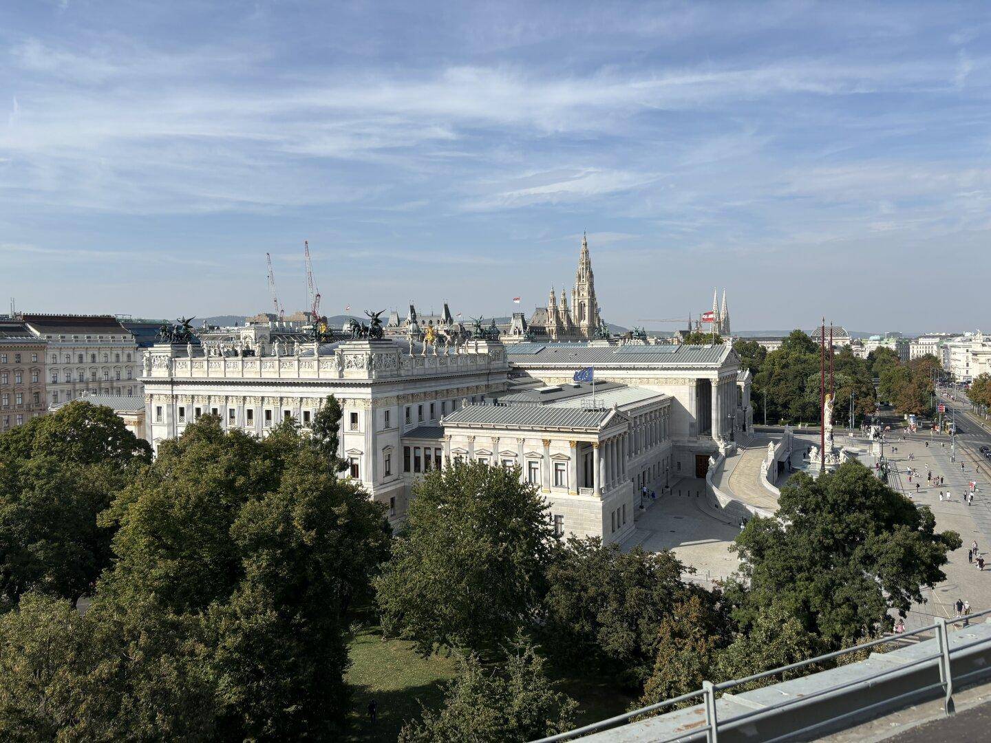 Weitläufiger Stadtblick über historische Gebäude, grüne Bäume und den blauen Himmel.