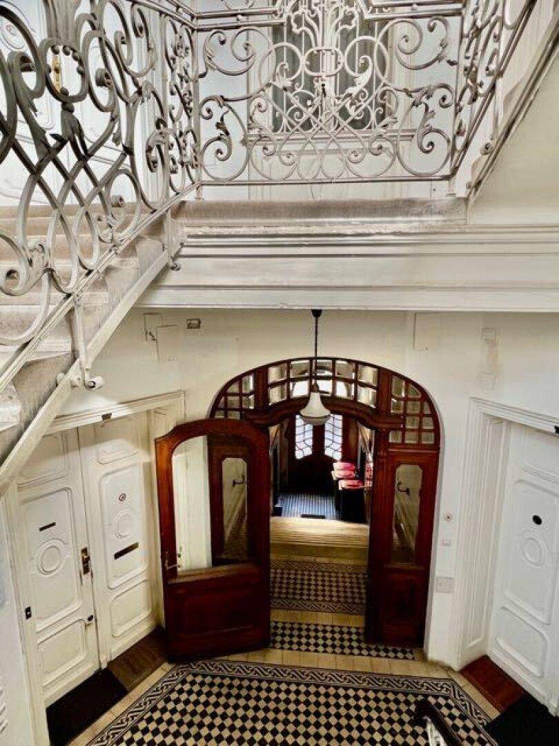 Elegantes Treppenhaus mit schmiedeeisernem Geländer, Holztüren und kariertem Fliesenboden.