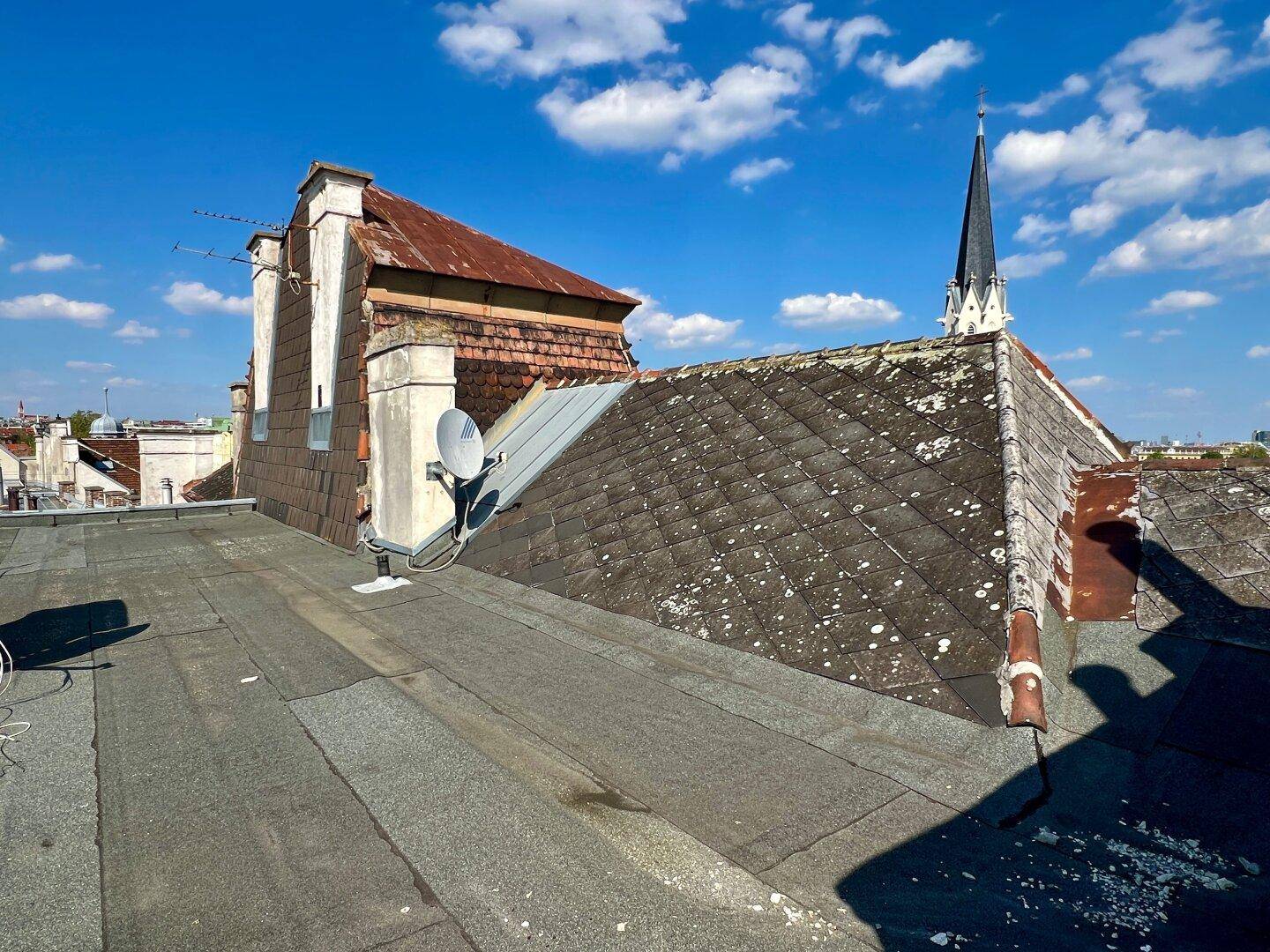 Detailansicht von alten Ziegeldächern und einem Flachdach mit Satellitenschüsseln.