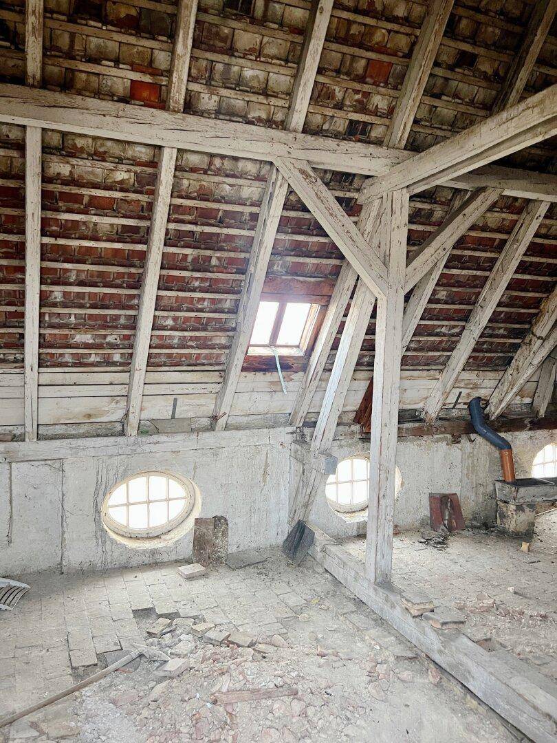 Unausgebauter Dachboden mit sichtbaren Holzbalken, runden Fenstern und viel Potenzial.