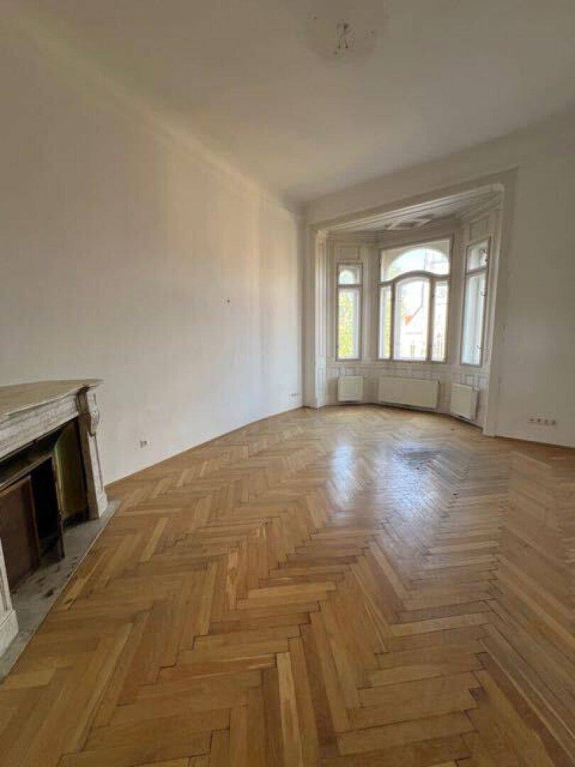 Helles Zimmer mit Fischgrätparkett, Erkerfenster und einem dekorativen Kaminsims.