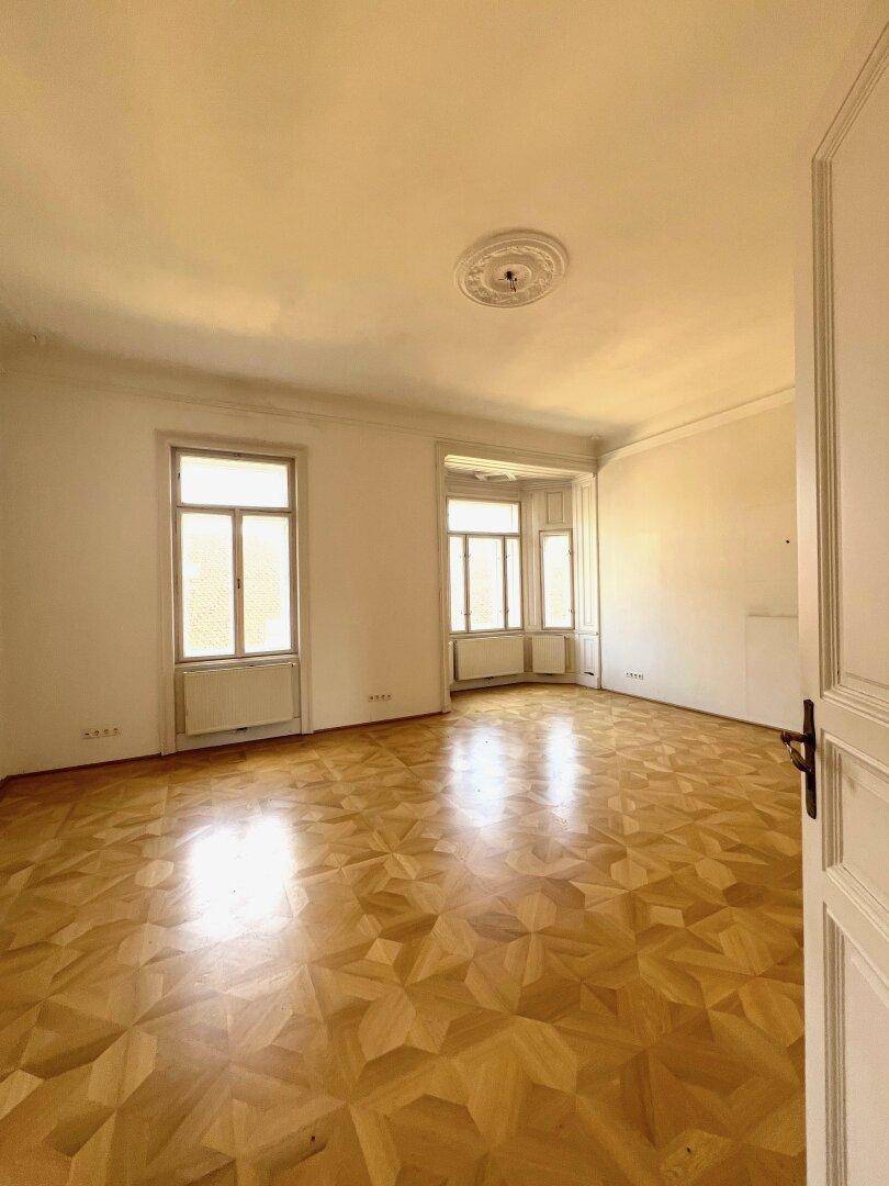 Geräumiges Zimmer mit geometrischem Parkettboden und einer Stuckrosette an der Decke.
