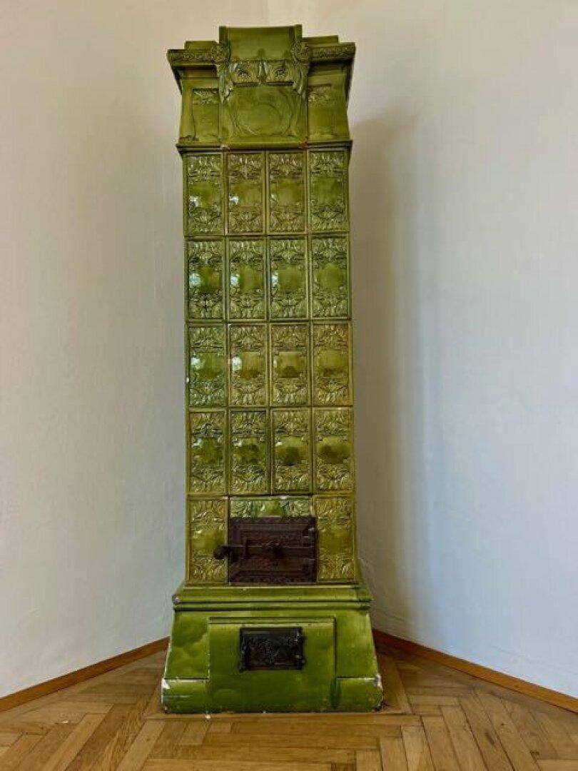 Großer, kunstvoll verzierter grüner Kachelofen als traditionelle Heizquelle.