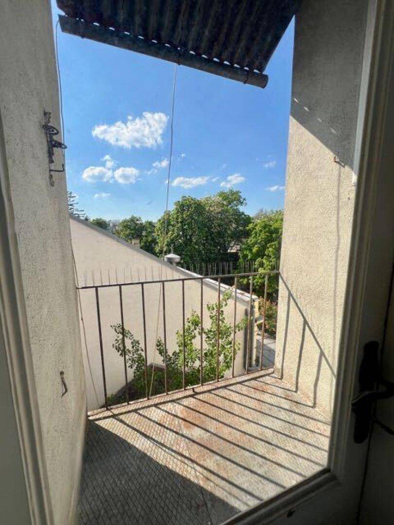 Kleiner Balkon mit Metallgeländer und Blick auf grüne Bäume unter blauem Himmel.