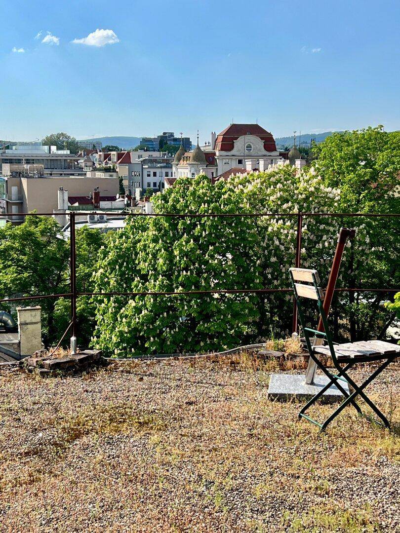 Dachterrasse mit einfacher Bestuhlung und weitem Blick über die Stadt und grüne Bäume.