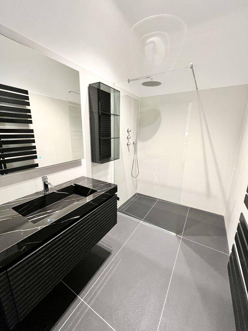 Luxuriöses Badezimmer mit großer begehbarer Dusche, Doppelwaschbecken und eleganten schwarzen Marmoroberflächen.