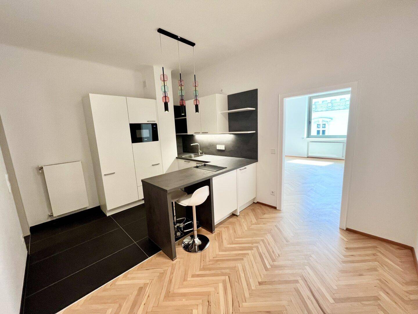 Moderne Einbauküche mit weißen Fronten, dunkler Arbeitsplatte und einer praktischen Kücheninsel mit Barhocker.