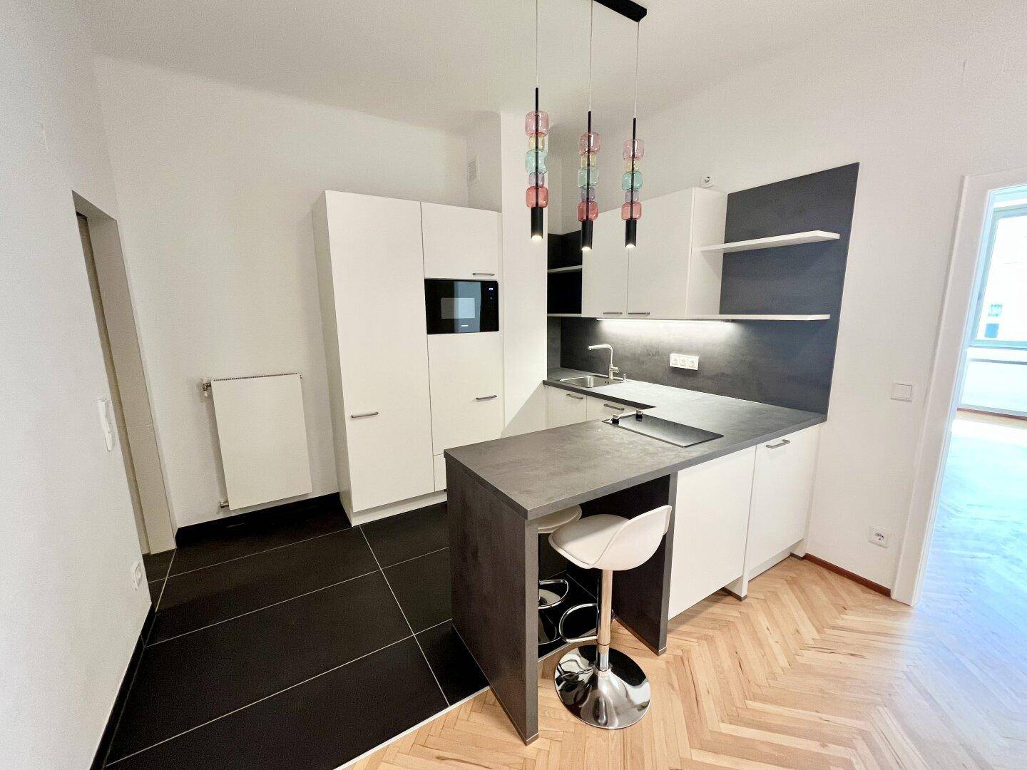Kompakte, moderne Küche mit integrierten Geräten, dunkler Arbeitsplatte und Bartresen.