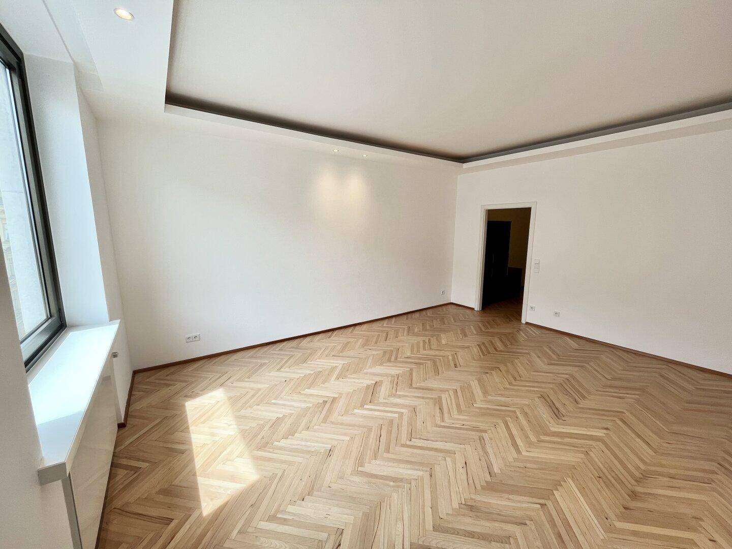 Geräumiges, helles Zimmer mit Fischgrätparkett und Zugang zu einem weiteren Bereich.