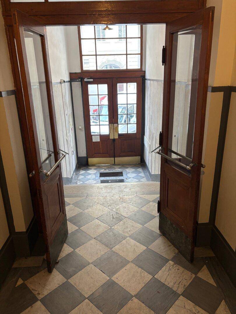 Eingangsbereich mit doppelten Holztüren, Oberlicht und gefliestem Schachbrettmuster-Boden in einem Altbau.