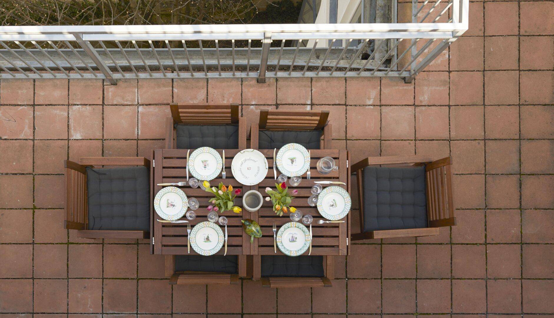 Von oben gesehener, gedeckter Esstisch auf einer gefliesten Dachterrasse.