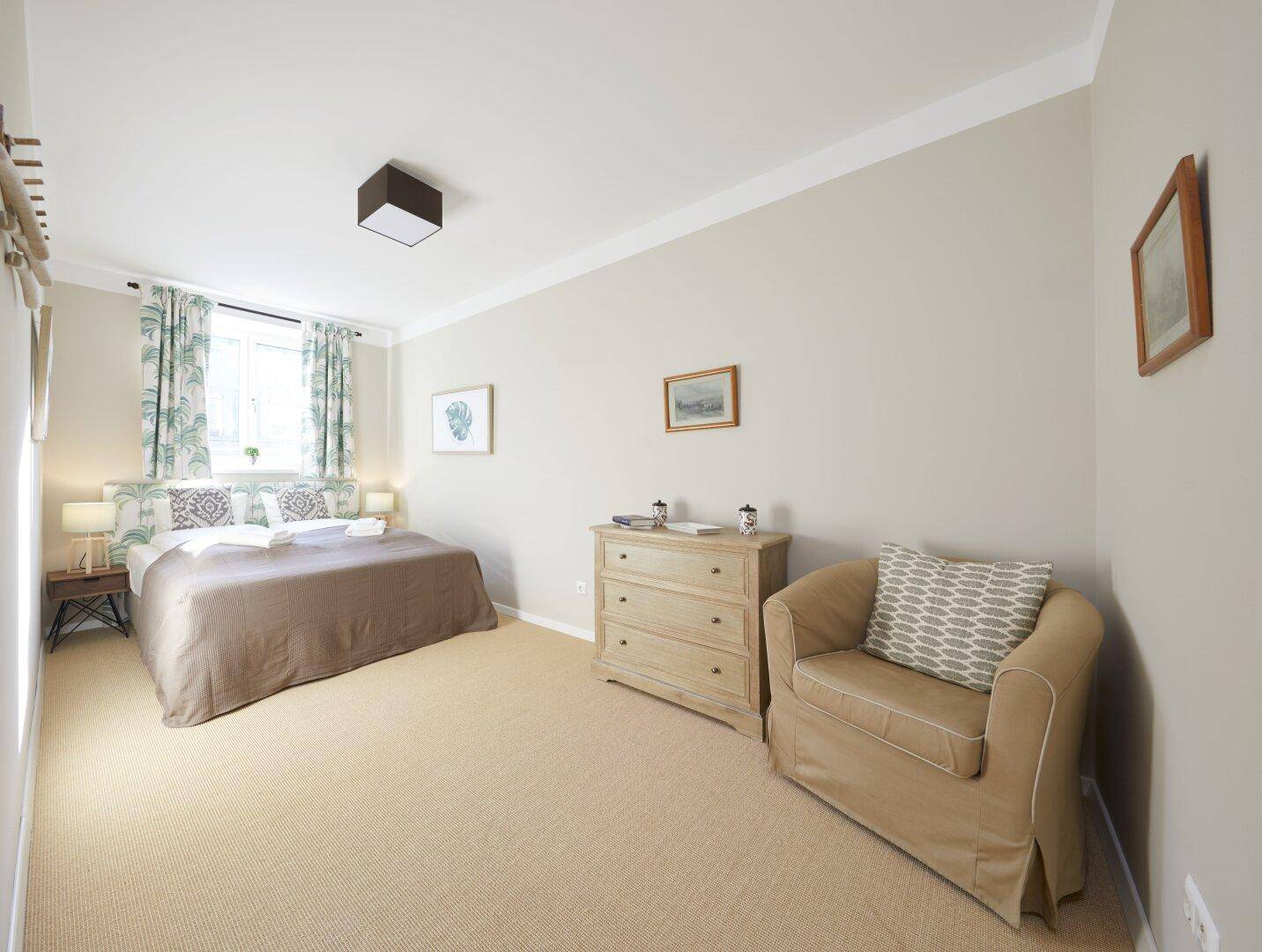 Helles Schlafzimmer mit Teppichboden, Doppelbett und schlichter, moderner Einrichtung.