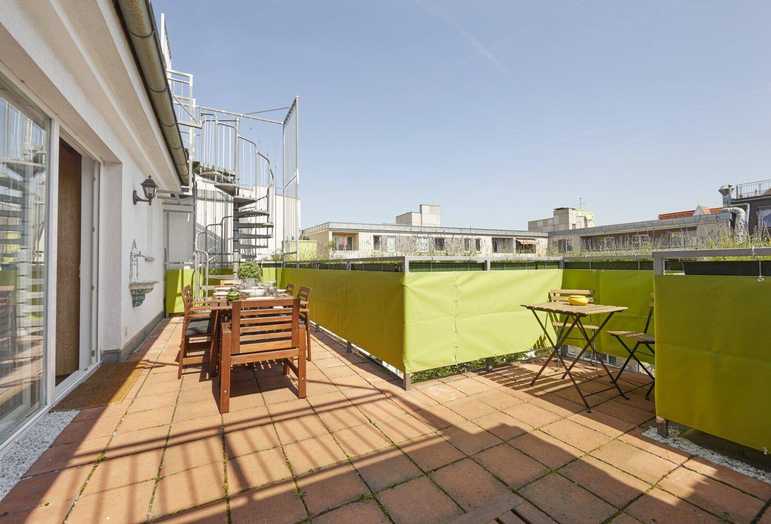 Weitläufige Dachterrasse mit Essbereich, Sonnenschutz und Wendeltreppe zum oberen Bereich.