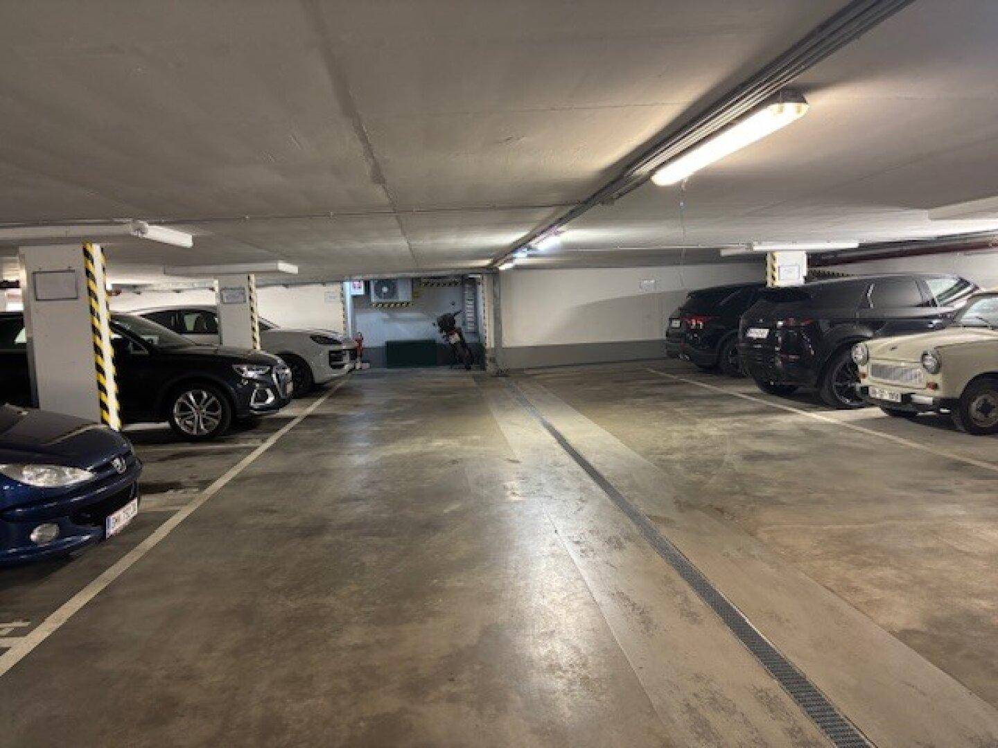 Helle Tiefgarage mit markierten Stellplätzen und verschiedenen Fahrzeugen.