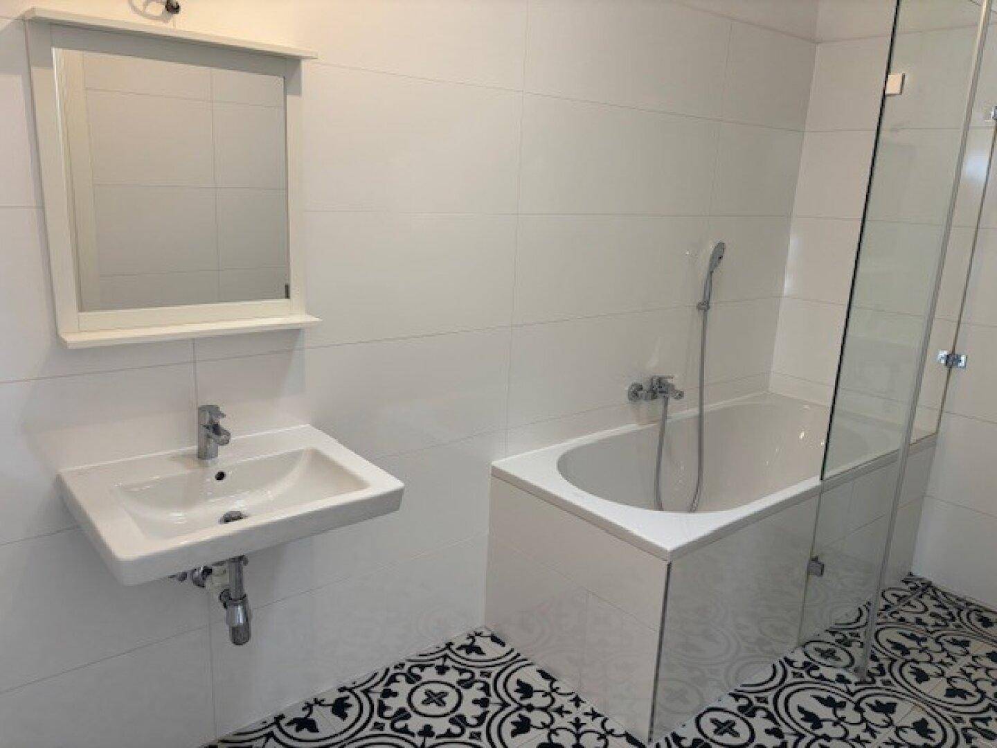 Modernes Badezimmer mit Badewanne, Duschabtrennung und auffälligen schwarz-weißen Fliesen.