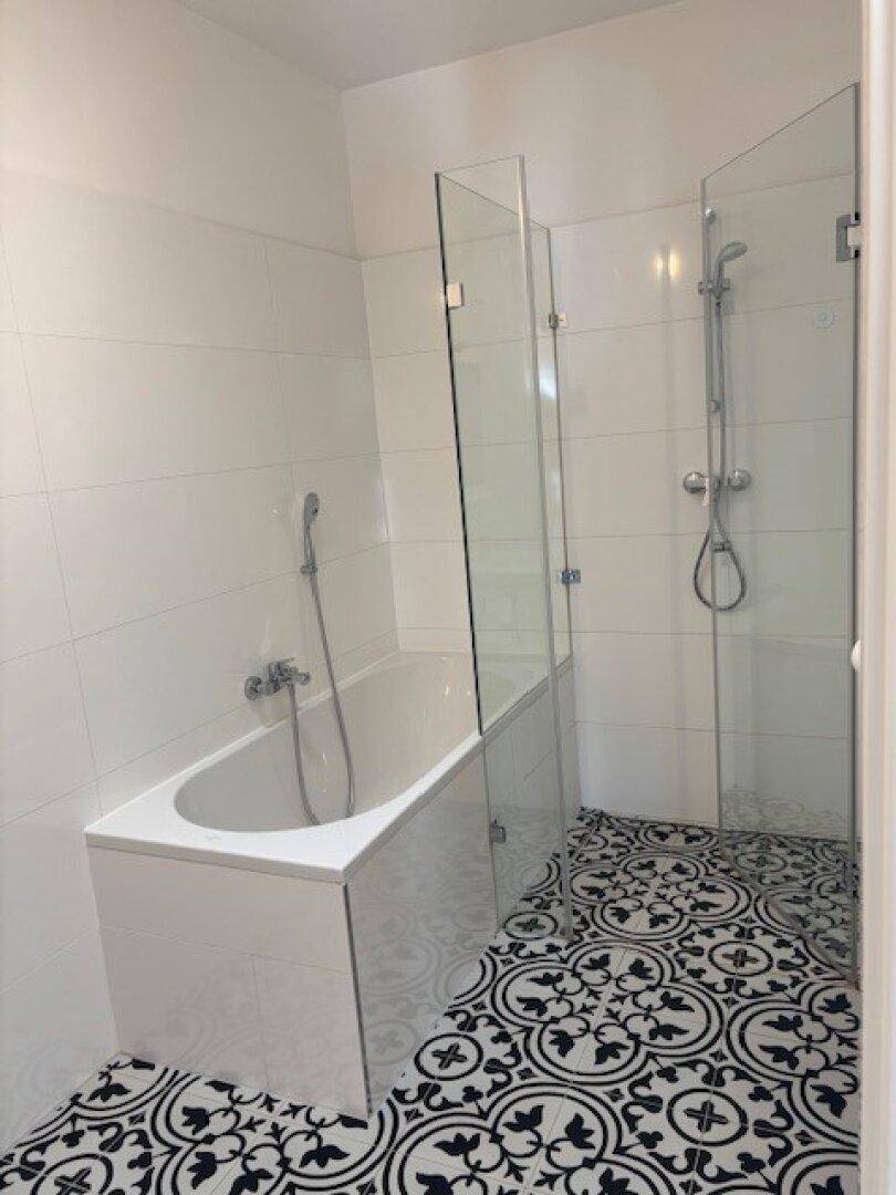 Helles Badezimmer mit Badewanne, Duschbereich und stilvollen schwarz-weißen Bodenfliesen.