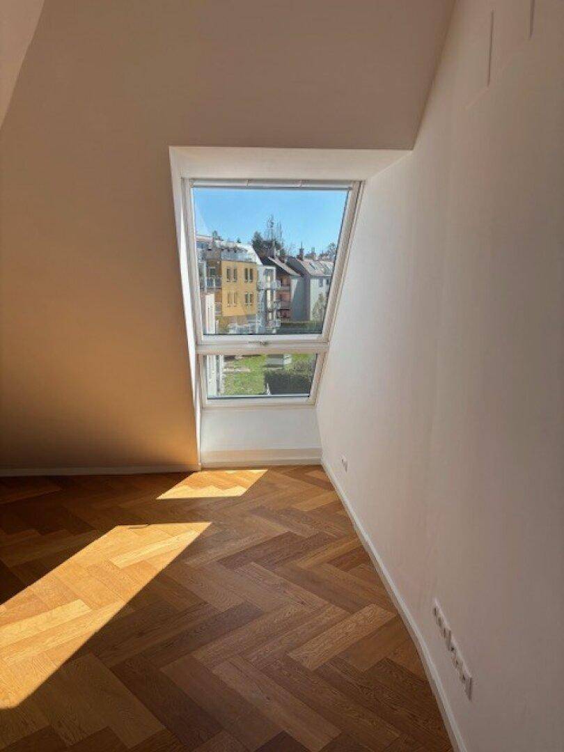 Gemütliches Zimmer im Dachgeschoss mit großem Dachfenster und hellem Fischgrätparkett.