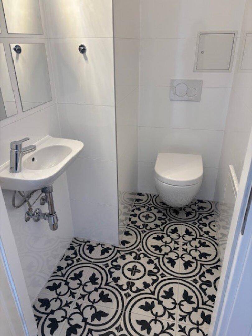 Separates Gäste-WC mit Wand-WC, kleinem Waschbecken und dekorativen Bodenfliesen.