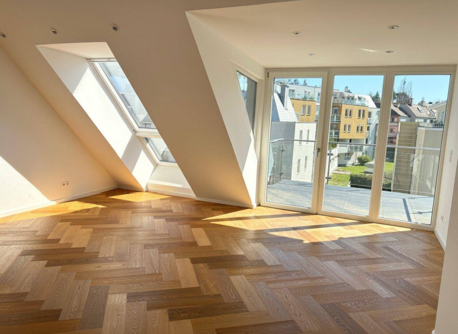 Lichtdurchfluteter Raum mit schrägem Dachfenster, Balkonzugang und elegantem Fischgrätparkett.
