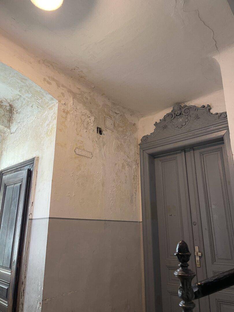 Detailansicht einer Wand im Flur mit abblätternder Farbe und einem verzierten Türrahmen.