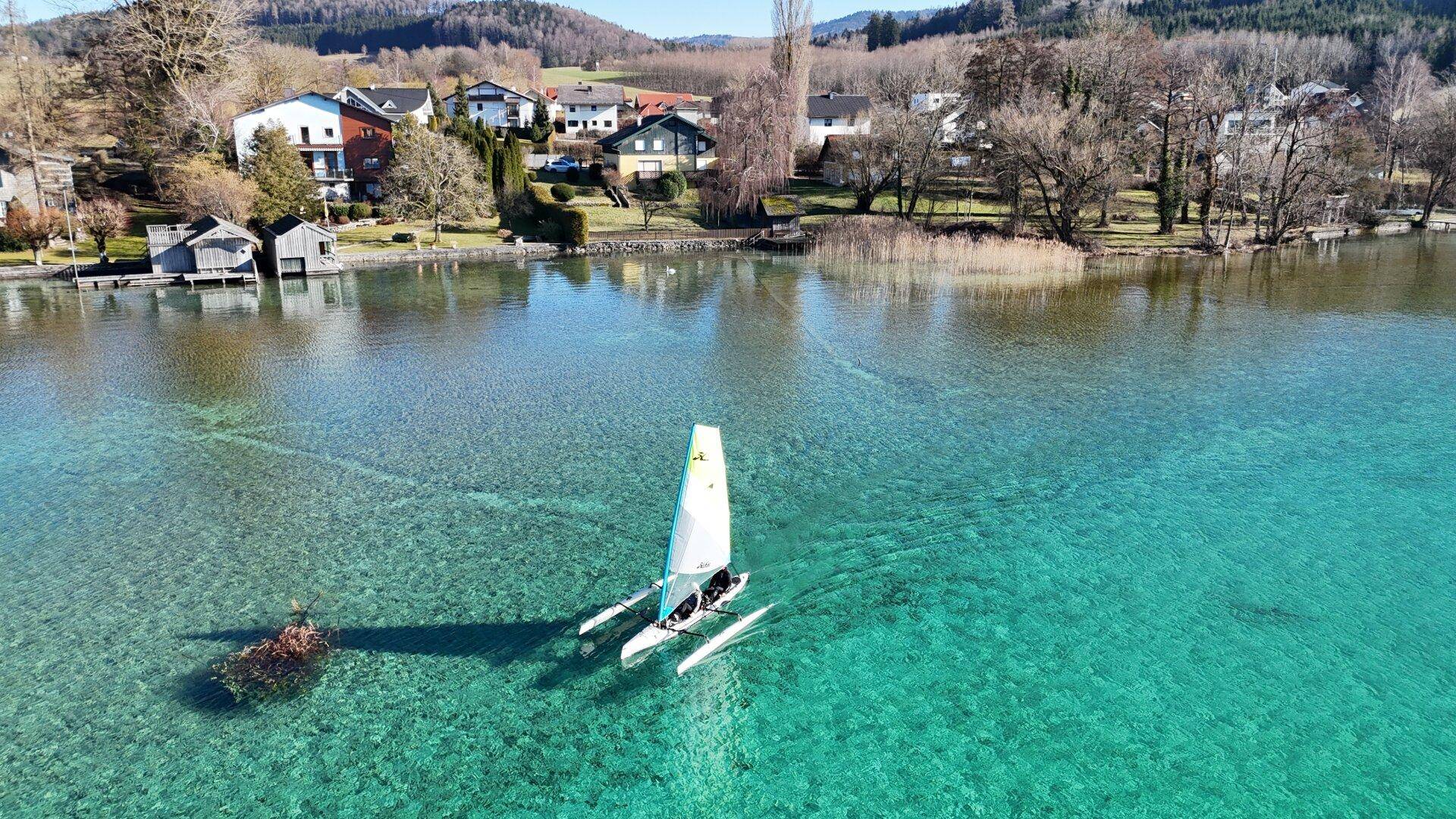 Klarer Attersee mit Segelboot und Blick auf die umliegende Uferlandschaft und Häuser.