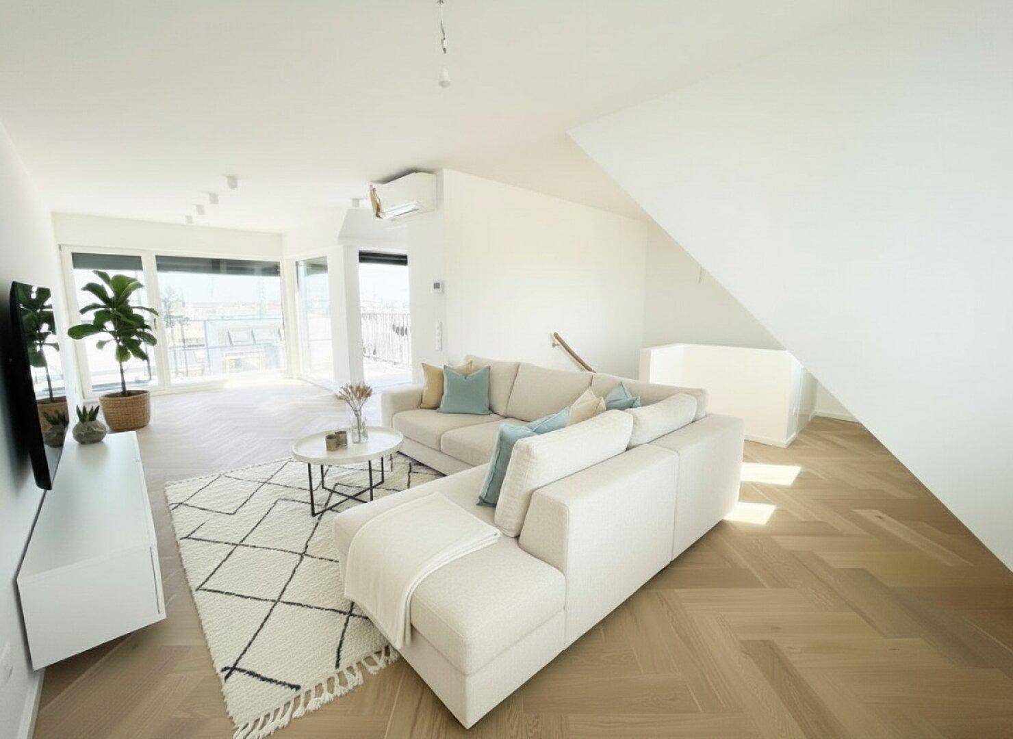 Modern eingerichteter Wohnbereich mit beigem Sofa, Teppich und hellem Fischgrätparkett.