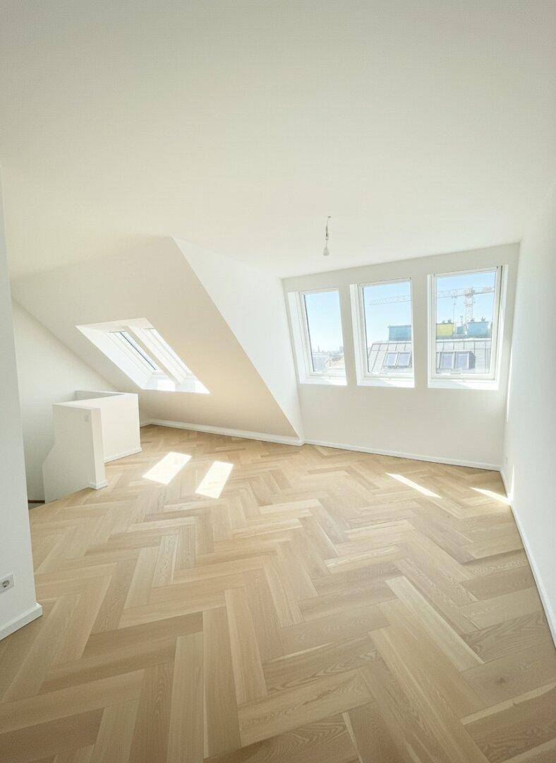 Helles Zimmer mit Fischgrätparkett, Dachschrägen und Dachfenstern für viel Tageslicht.