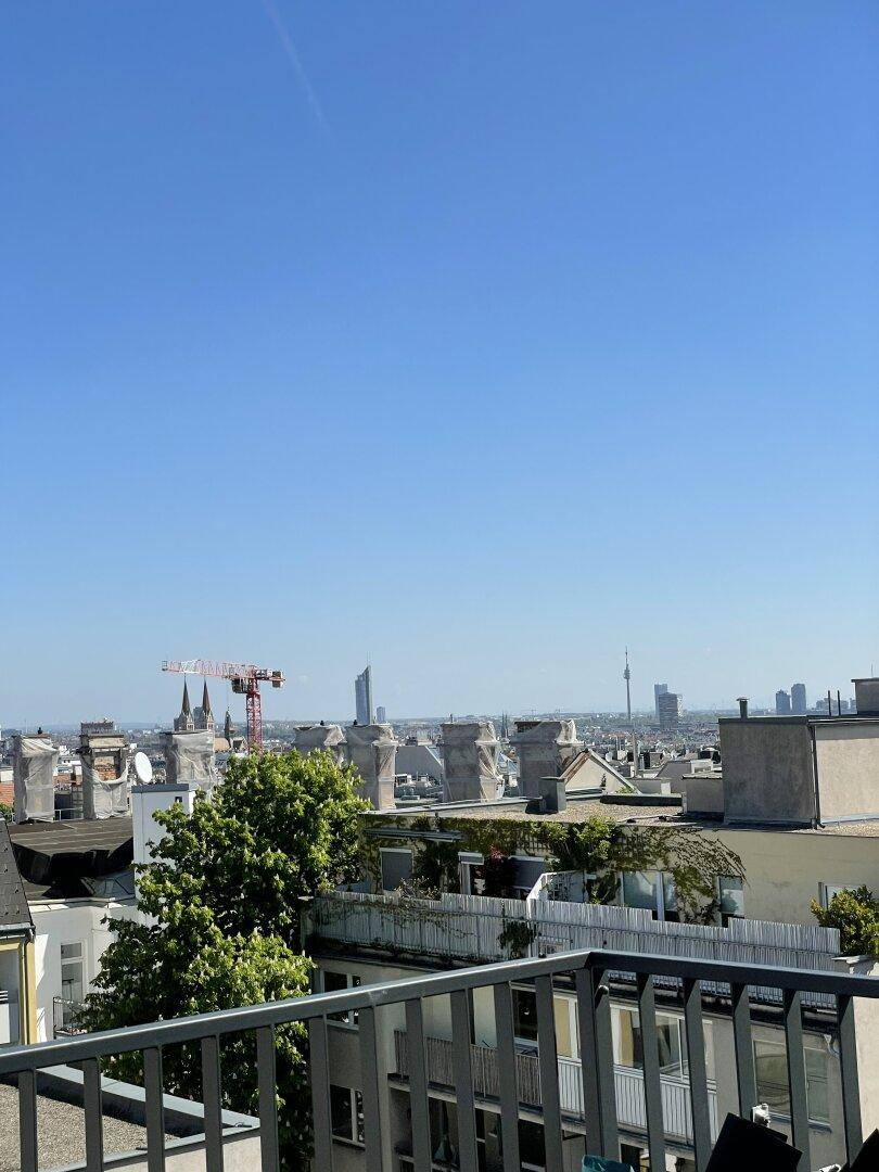 Weitblick über die Stadt von einem sonnigen Balkon mit urbaner Skyline.