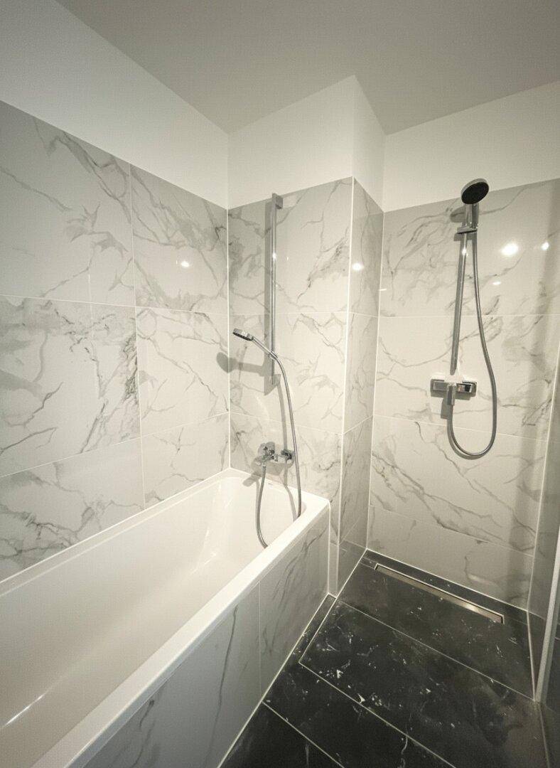 Modernes Badezimmer mit Badewanne, Dusche und eleganten Marmorfliesen an den Wänden.