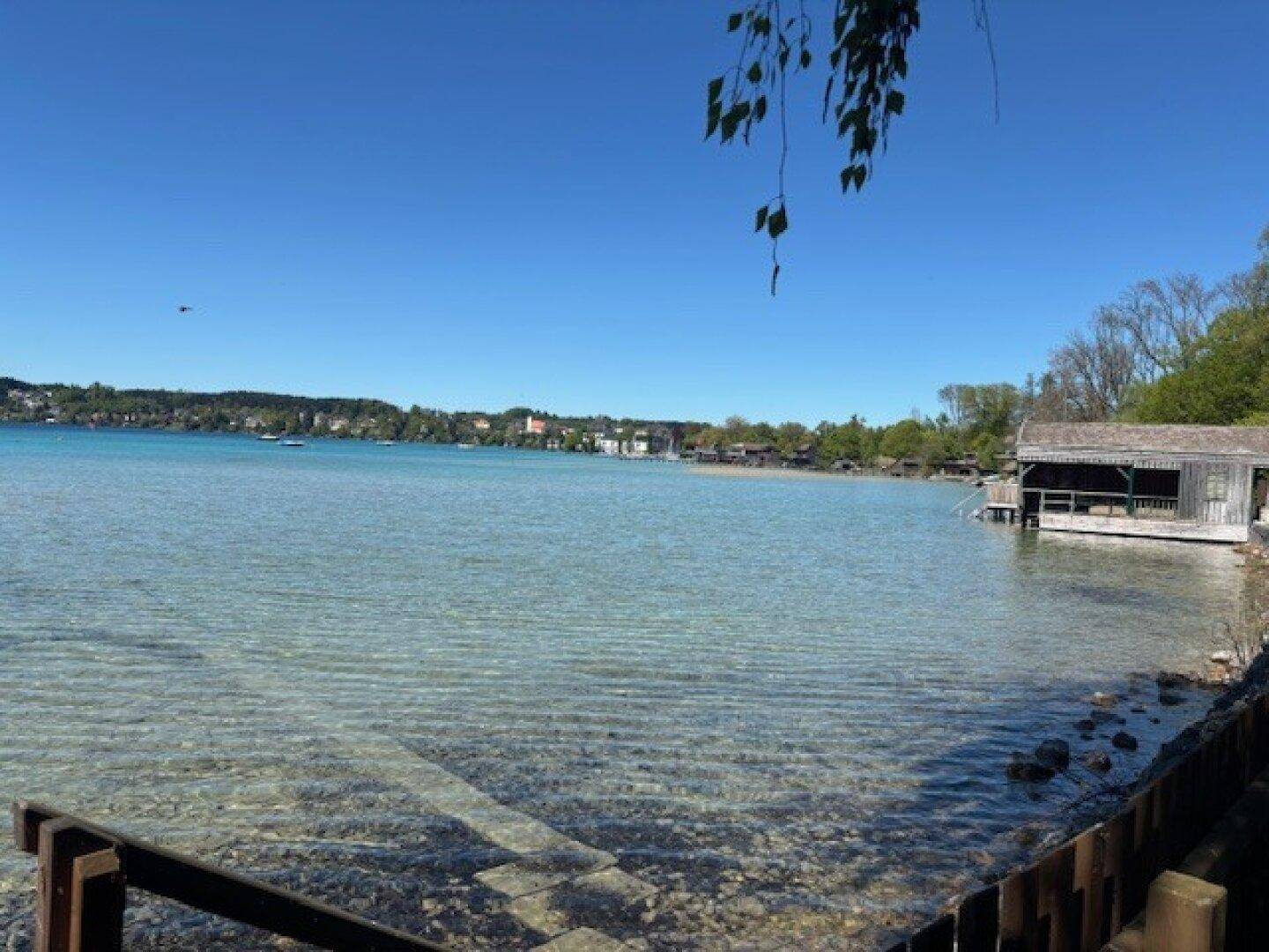 Ruhiger See mit klarem Wasser, einem Bootshaus am Ufer und üppiger Vegetation.