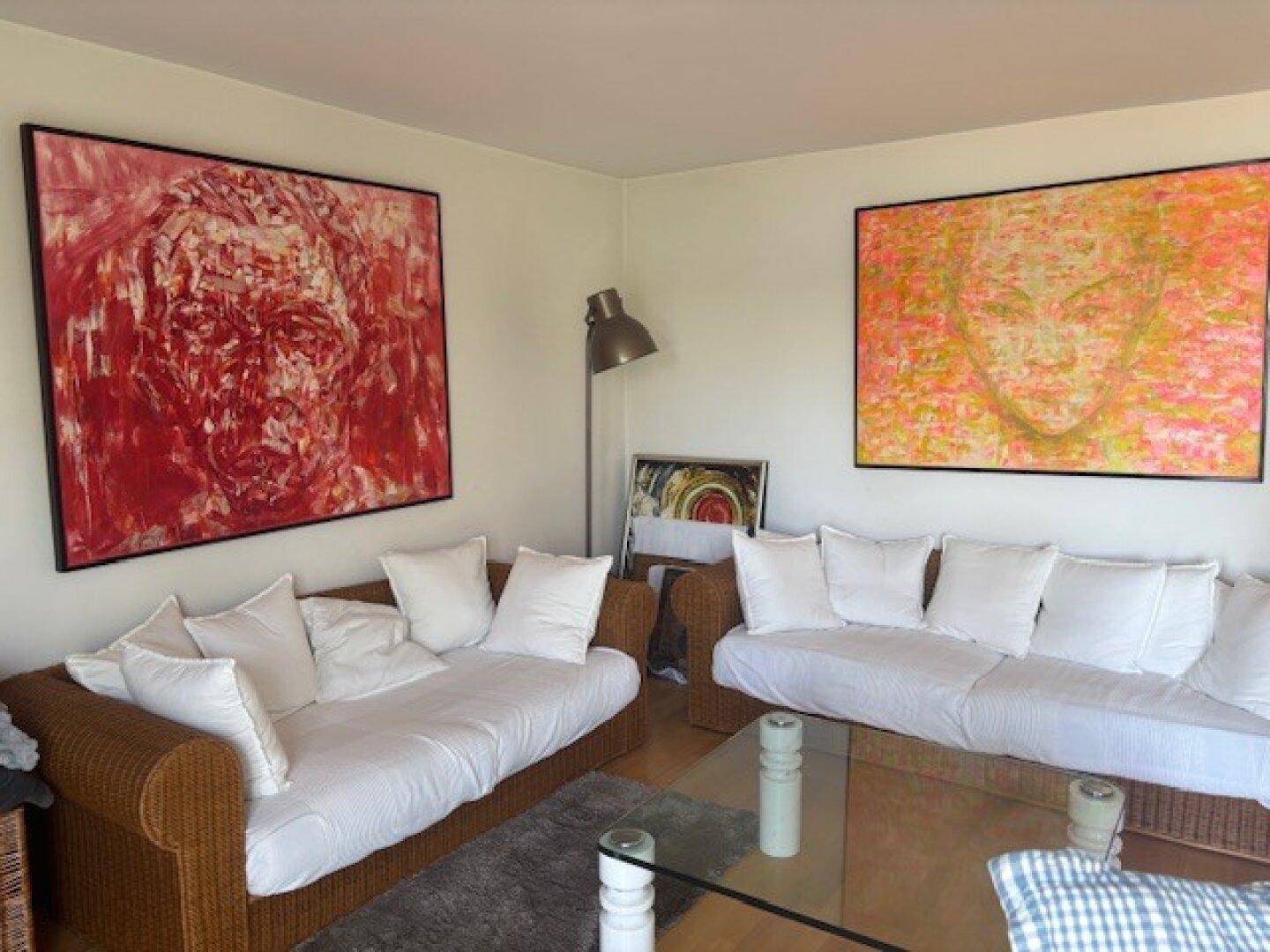 Helles Wohnzimmer mit zwei Sofas, modernen Kunstwerken und einem Couchtisch aus Glas.