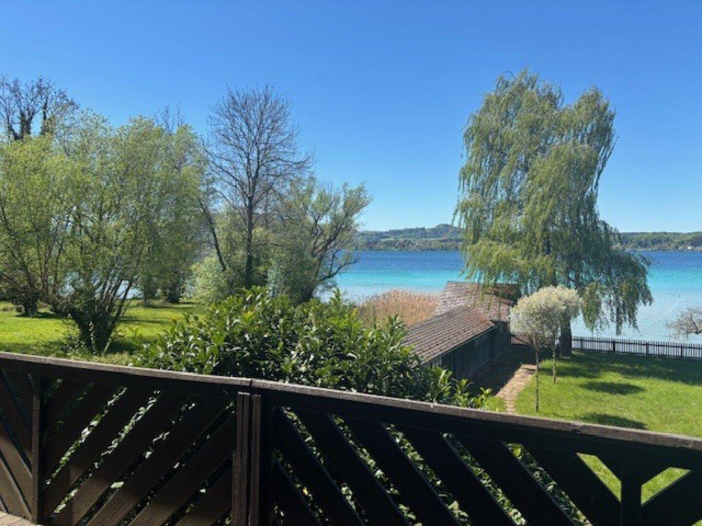 Panoramablick vom Balkon auf den See und den gepflegten Garten mit üppiger Vegetation.