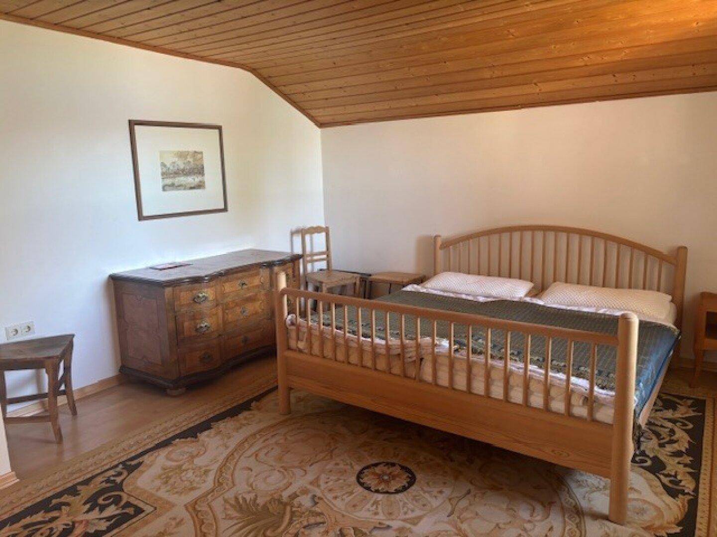 Geräumiges Schlafzimmer mit Holzbett, antiker Kommode und Teppichboden unter einer Holzdecke.