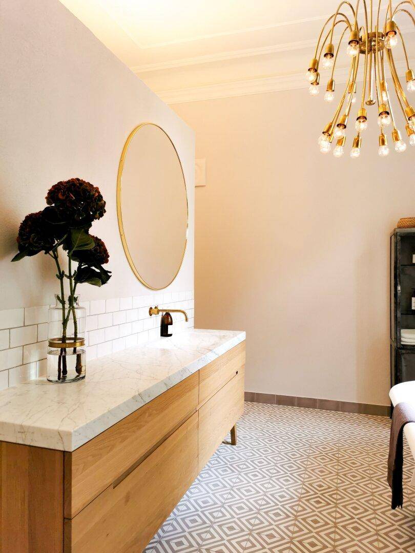 Elegantes Badezimmer mit Marmorwaschtisch, gemusterten Fliesen und goldenen Armaturen.