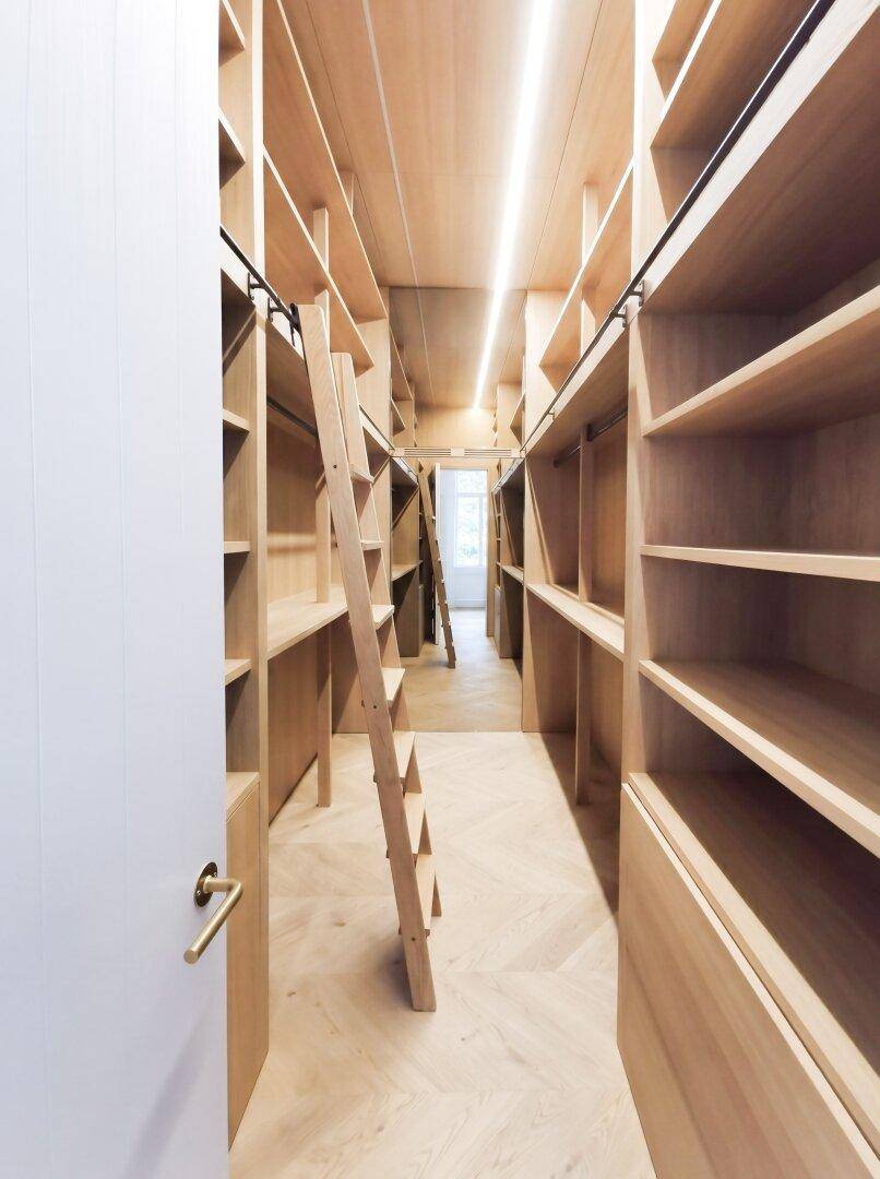 Geräumiger begehbarer Kleiderschrank mit Holzregalen und integrierter Beleuchtung.