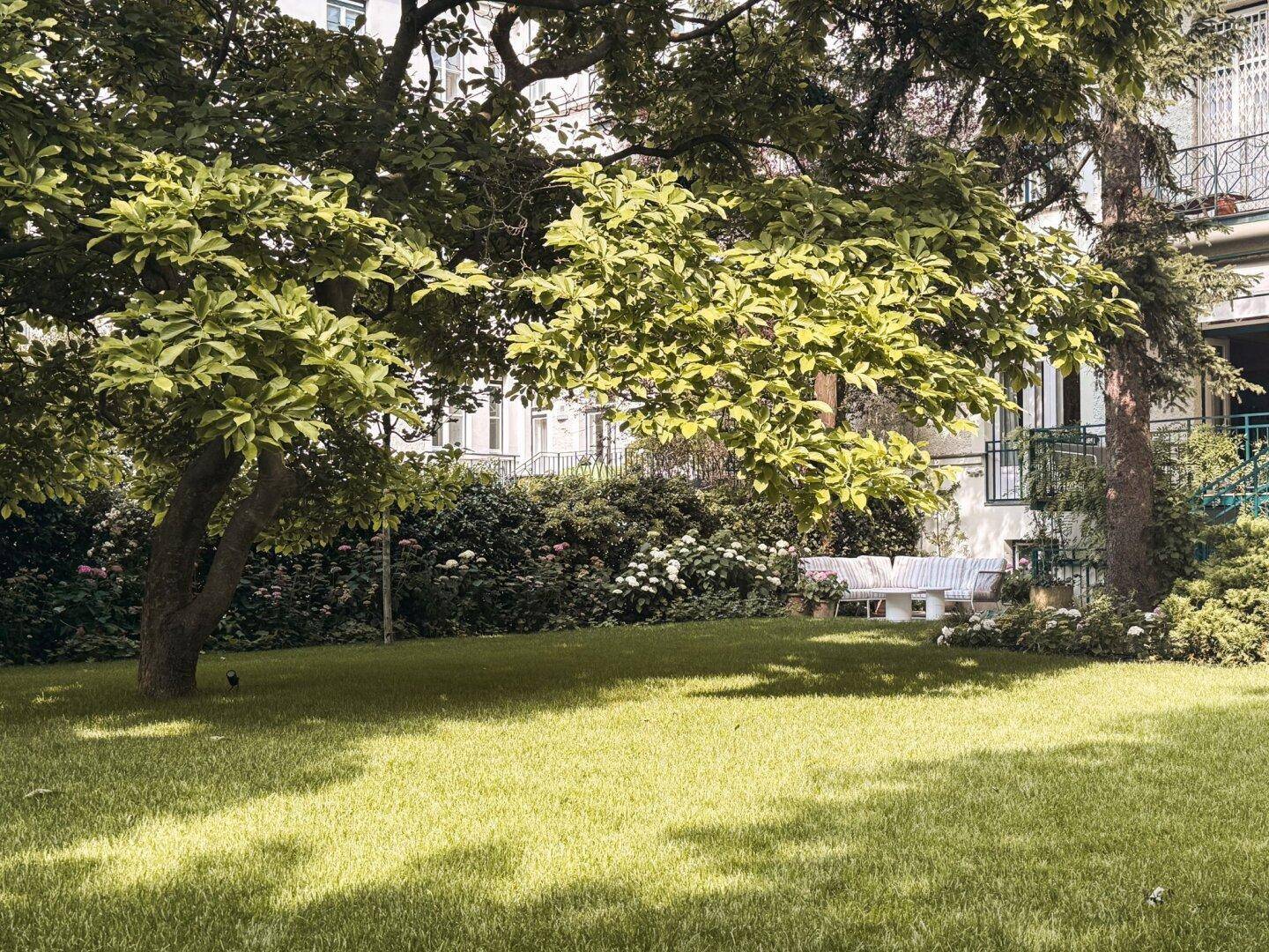 Grüner Gartenbereich mit Rasenfläche und großen Bäumen, ideal zum Entspannen im Freien.