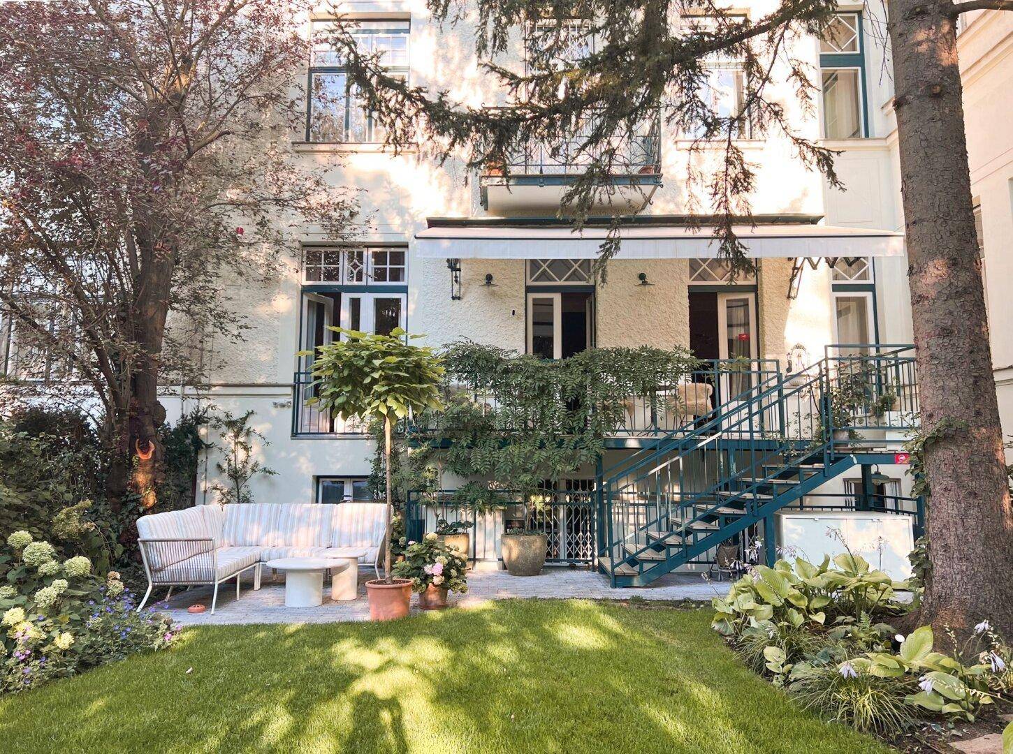 Gepflegter Garten mit Rasen, Terrasse und Außentreppe, die zum Gebäude führt.
