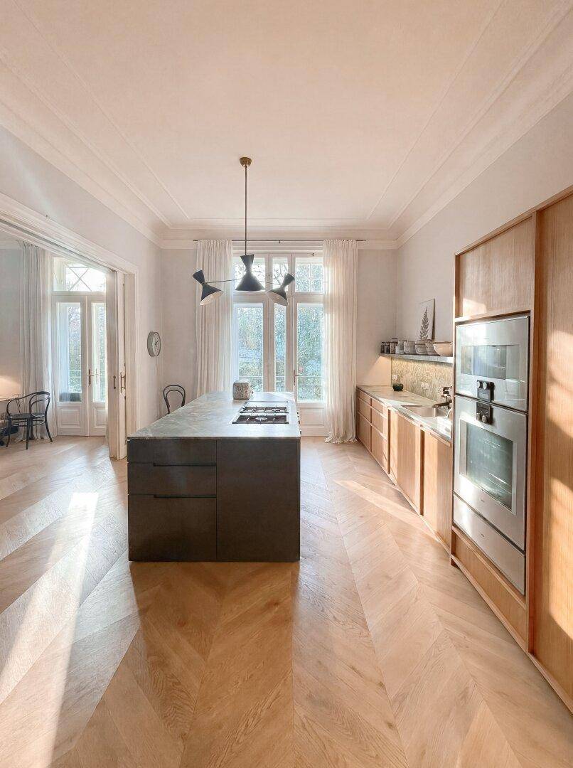 Geräumige, moderne Küche mit dunkler Kücheninsel, Holzboden und integrierten Geräten.