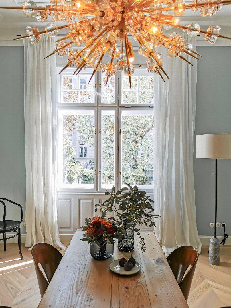 Eleganter Essbereich mit Holztisch, Kronleuchter und großen Fenstern mit Blick ins Grüne.