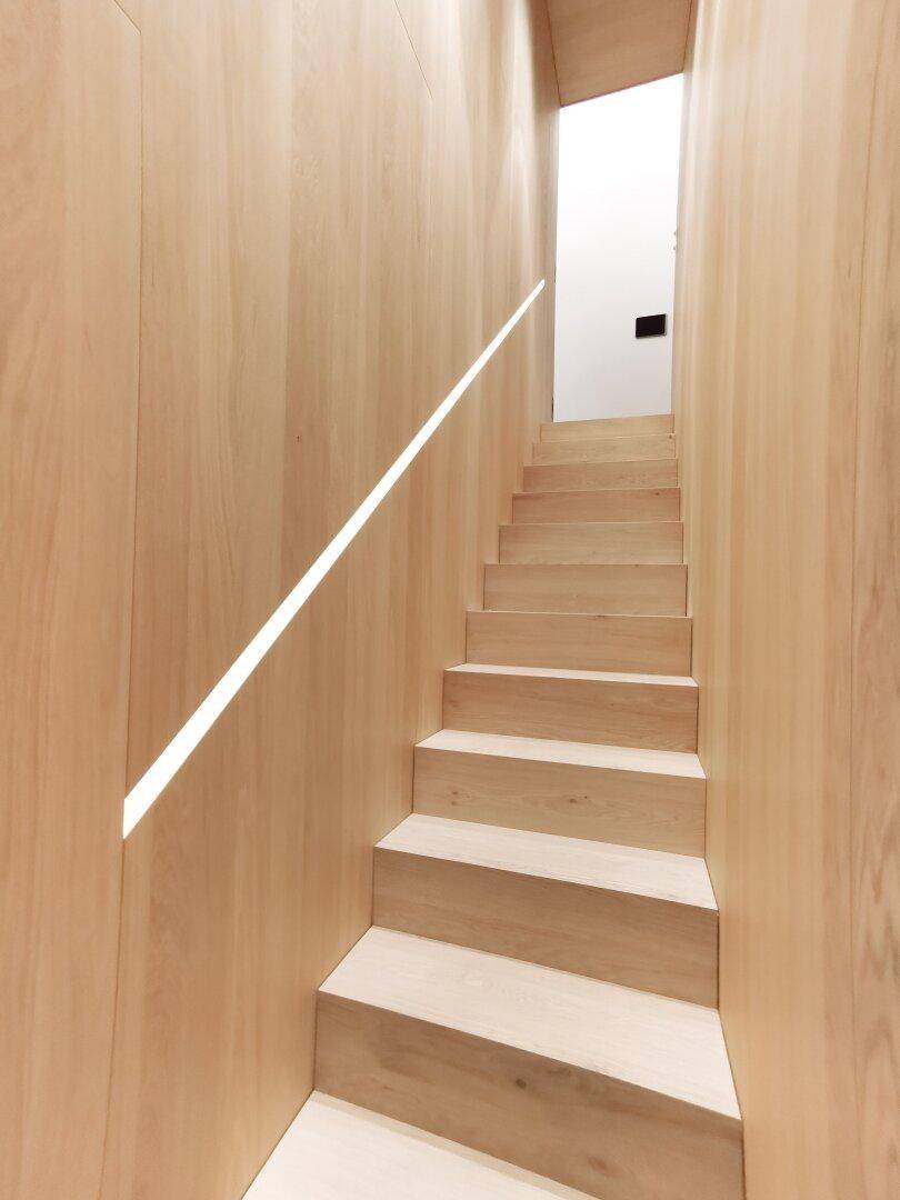 Heller Treppenaufgang mit Holzverkleidung und integrierter Beleuchtung, die nach oben führt.