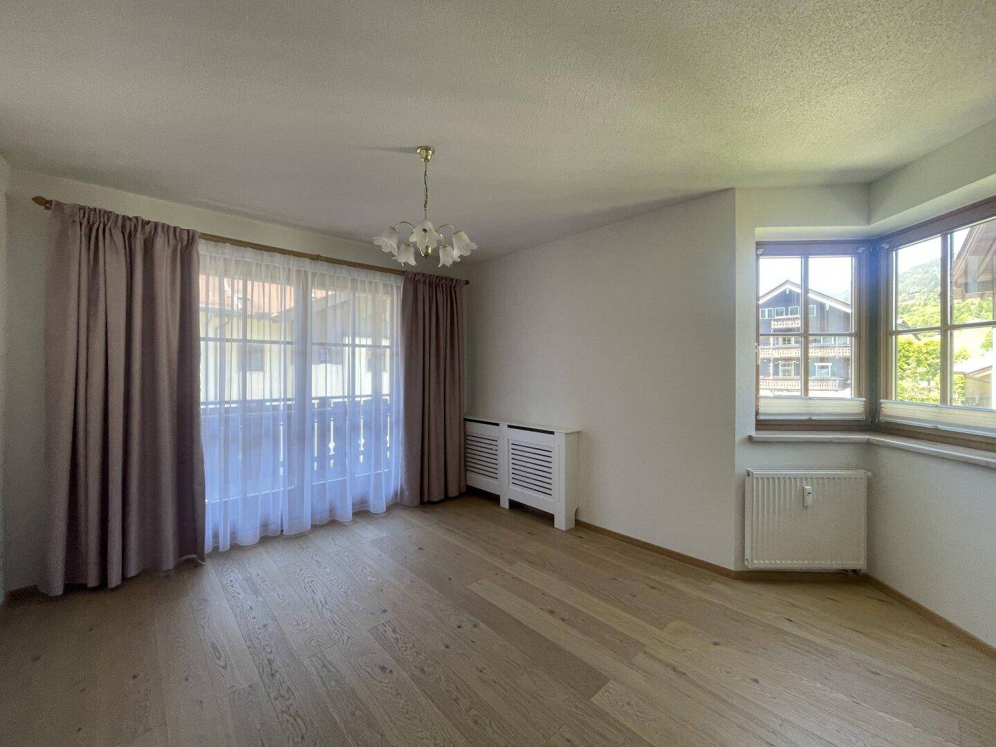 Geräumiges Zimmer mit Holzboden, großen Fenstern und Zugang zu einem französischen Balkon.