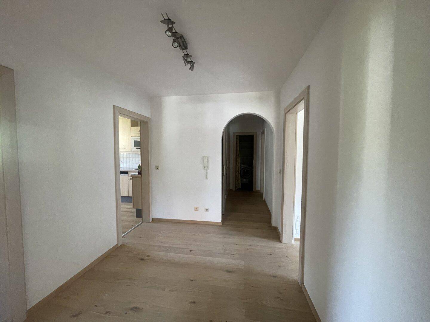 Langer Flur mit Holzboden und weiß gestrichenen Wänden, der verschiedene Zimmer verbindet.