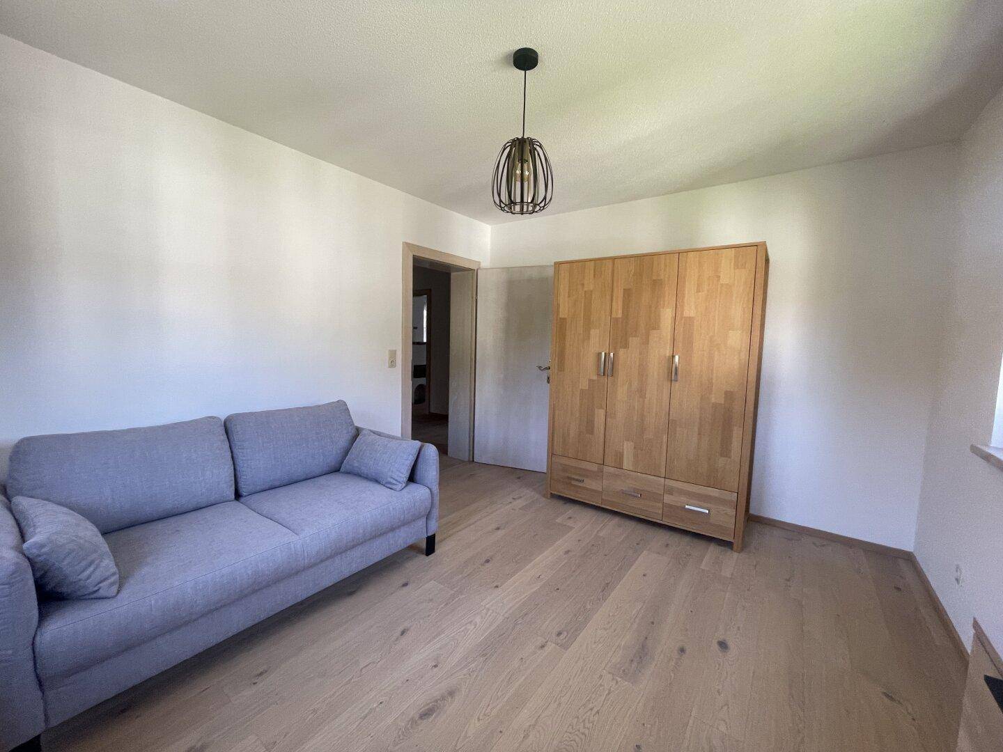 Schlafzimmer mit Holzboden, Sofa und einem Holzschrank, bietet eine angenehme Atmosphäre.