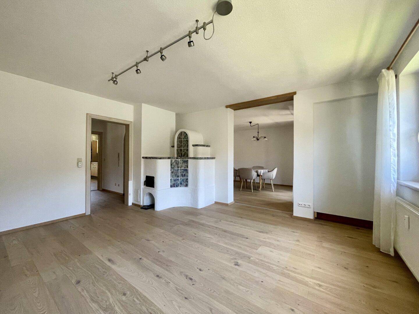 Geräumiges Wohnzimmer mit Holzboden und Kachelofen, der in den Essbereich übergeht.