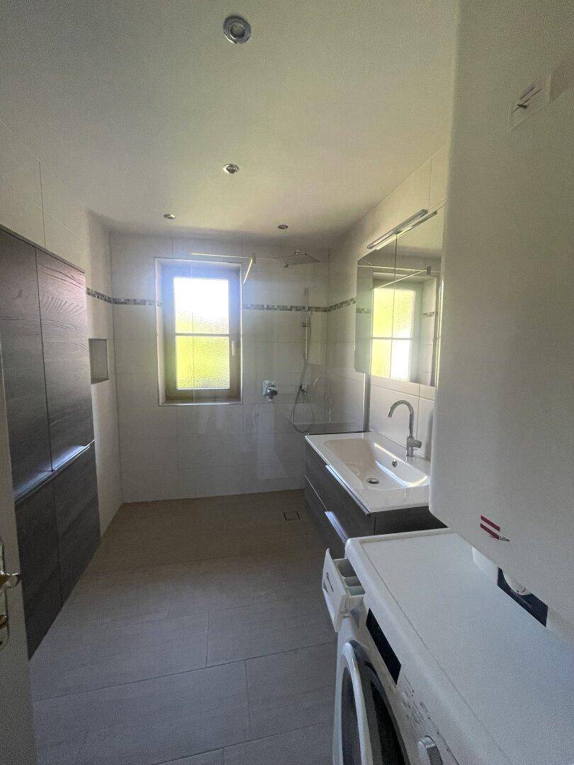 Modernes Badezimmer mit Dusche, Waschbecken und Fenster, inklusive Waschmaschine.