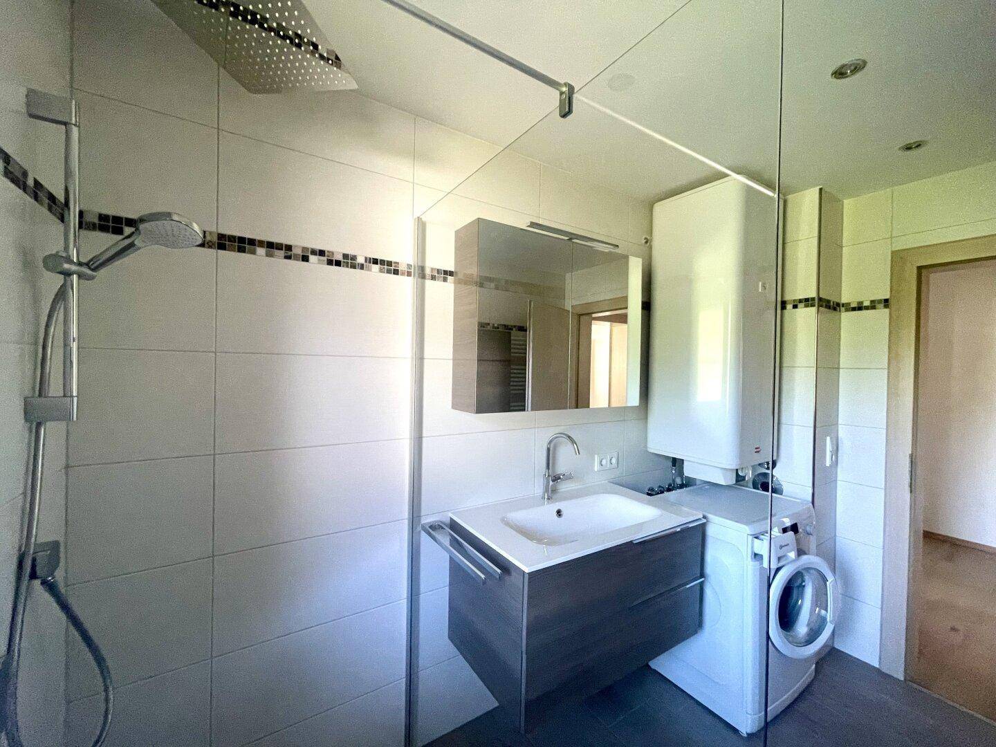 Helles Badezimmer mit ebenerdiger Dusche, Waschbecken und Spiegelschrank, gut gepflegt.