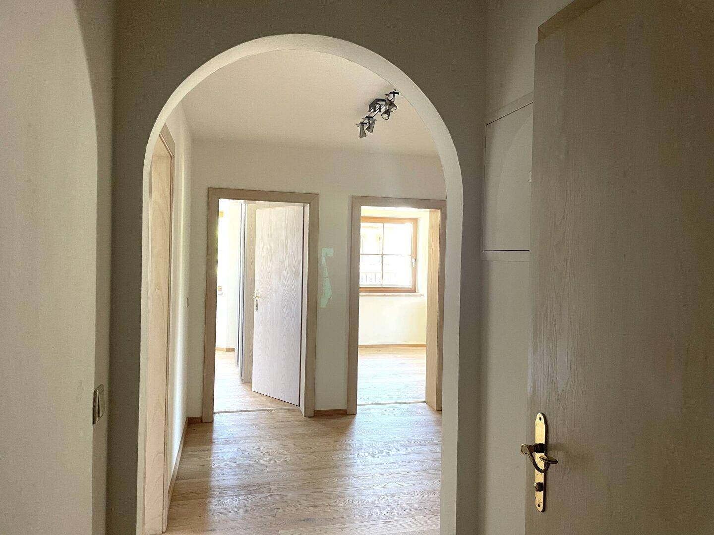 Heller Flur mit Holzboden und einem eleganten Rundbogen, der zu weiteren Räumen führt.